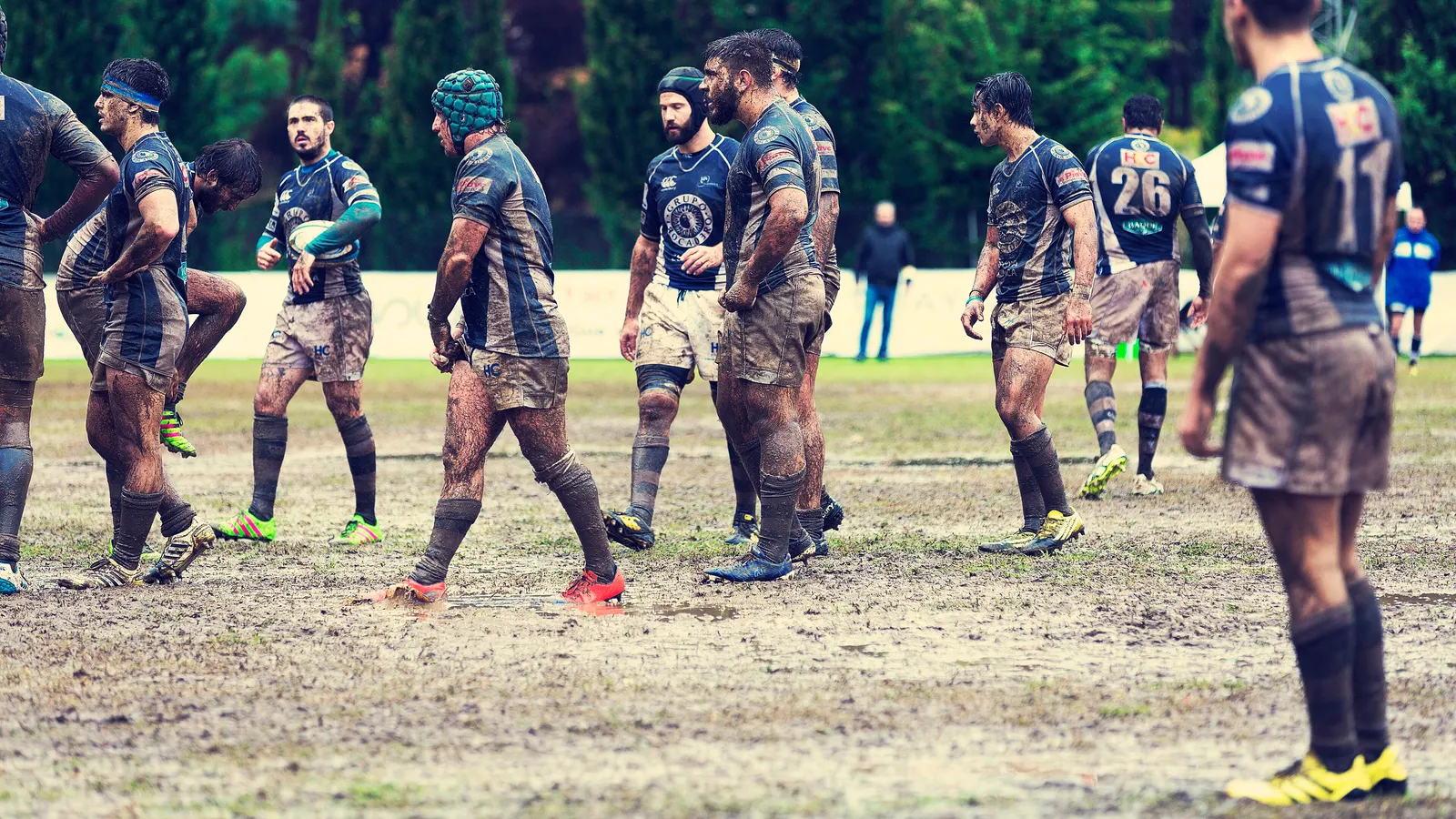 Joueurs de rugby couverts de boue sur un terrain détrempé, à l'arrêt entre deux phases de jeu